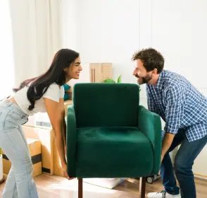 Pareja acomodando una poltrona en la sala de su vivienda nueva