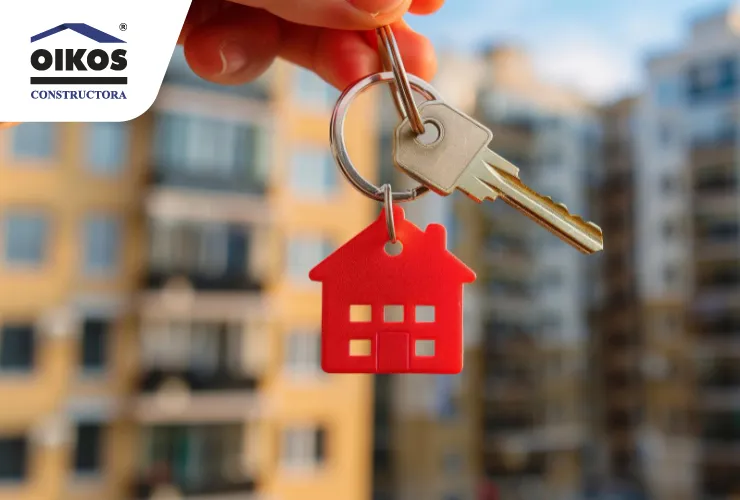 Conoce los beneficios de invertir en bienes raíces en el occidente de Bogotá Mano sosteniendo llaves de una vivienda con un edificio desenfocado al fondo