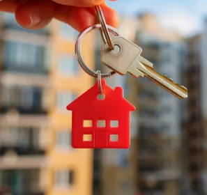 Mano sosteniendo llaves de una vivienda con un edificio desenfocado al fondo