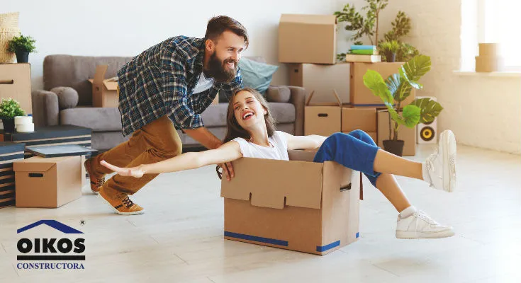 Pareja joven sonriente divirtiéndose con cajas de cartón en un apartamento nuevo