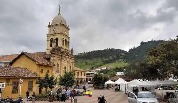 Iglesia principal y parque central de La Calera bajo un cielo nublado